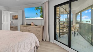 Ein Schlafzimmer mit einem großen Fernseher, einem Balkon mit Blick auf den Strand und einem Korbuschein-Kommoden.