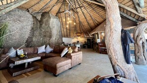A spacious living area with a high thatched ceiling, large rock formations, and a cozy seating arrangement. - Timbila Game Lodge (Phalaborwa)
