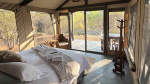 A spacious tented room with a large bed, a chair, and a table. - Timbila Game Lodge (Phalaborwa)