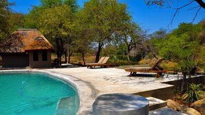 A swimming pool with lounge chairs and a small hut. - Timbila Game Lodge (Phalaborwa)
