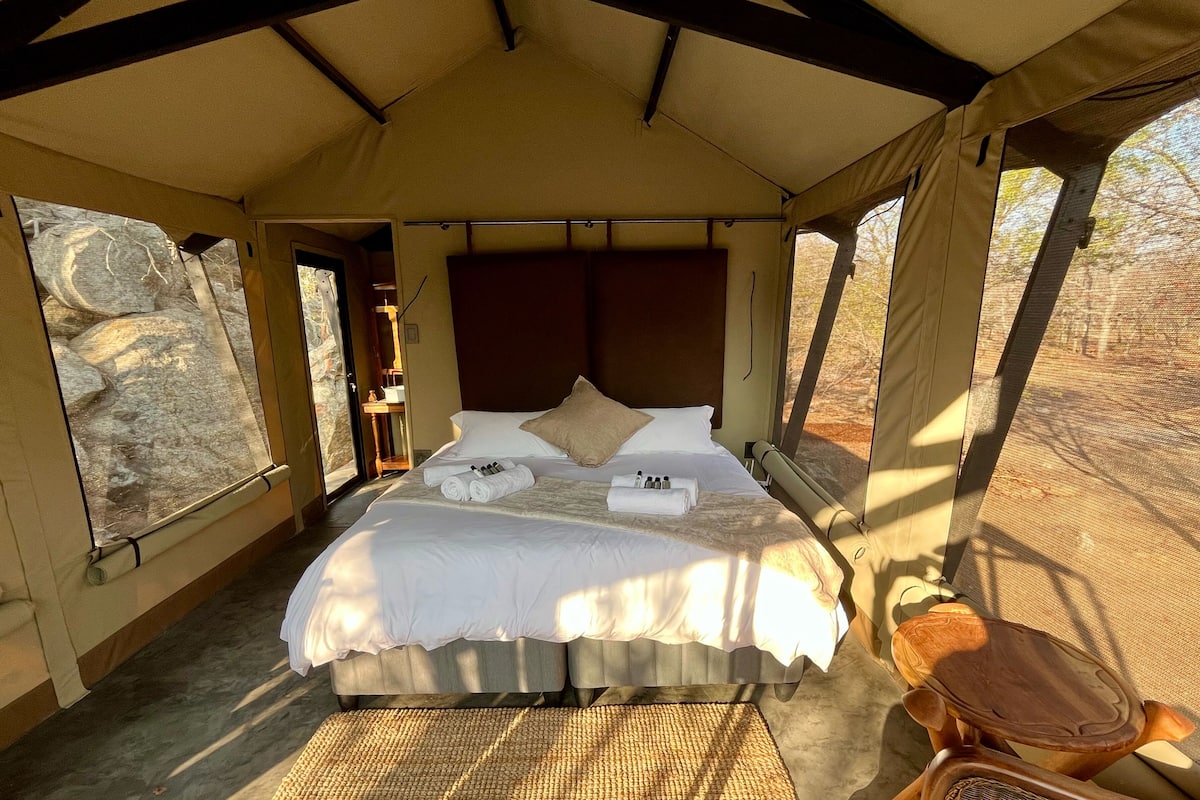 A tented accommodation with a bed, towels, and a chair.