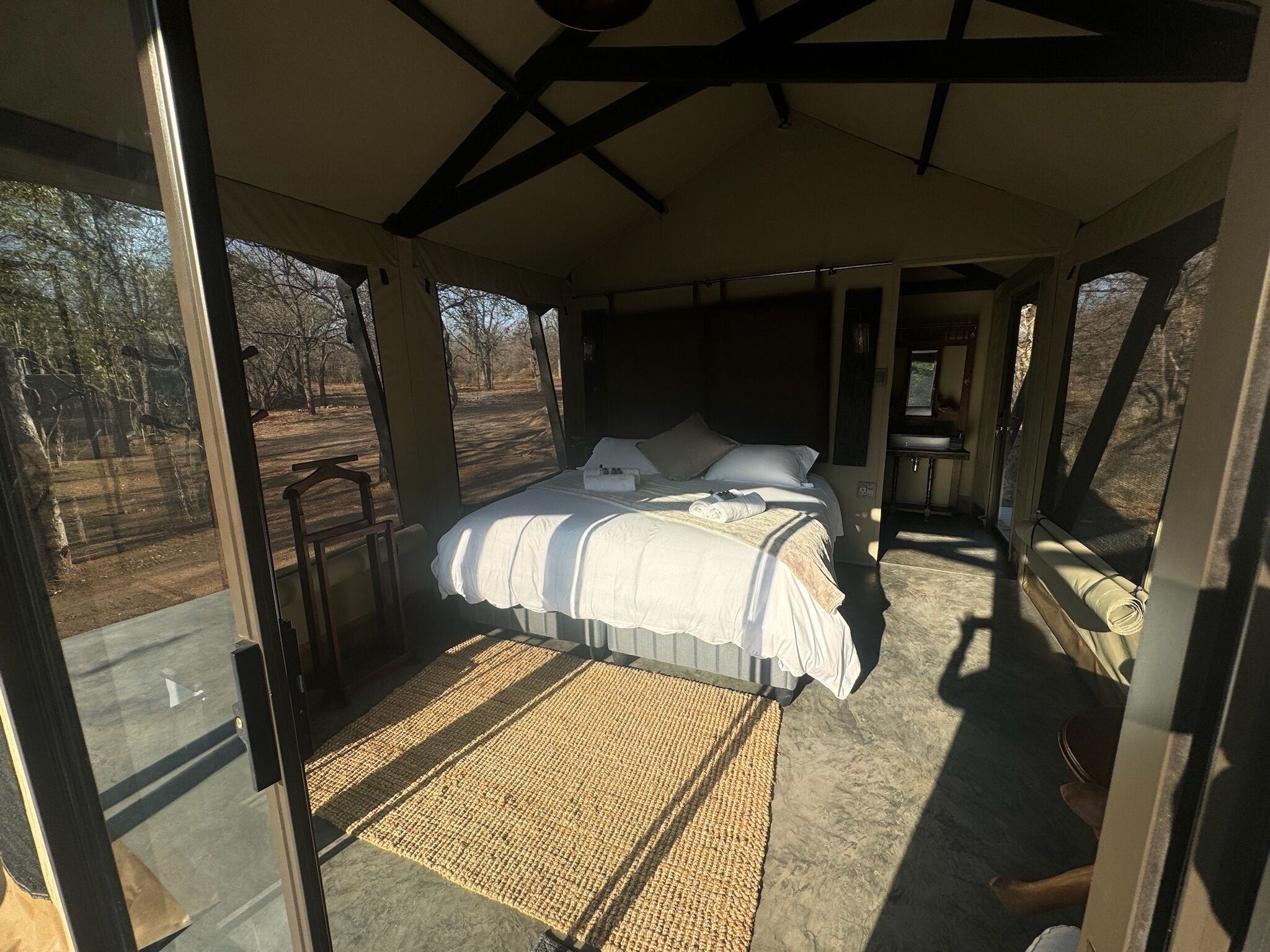 Uma ampla sala com tenda, uma cama grande, uma mesinha e vista para o exterior.