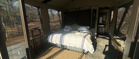 Amplia habitación con tienda, una cama grande, una mesita y vistas al exterior.