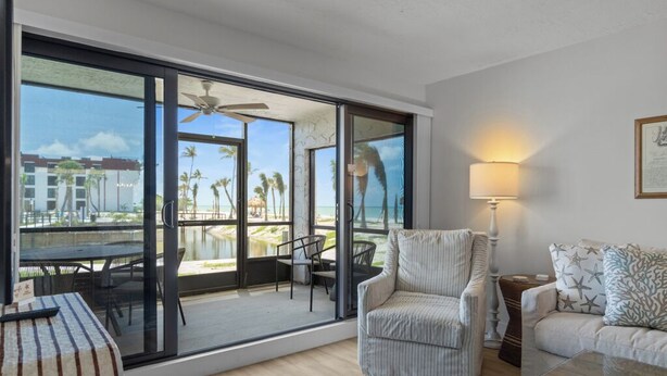A spacious living room with a large sliding glass door leading to a balcony with a view of palm trees and a beach.