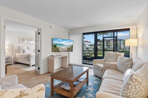 Un salon moderne avec une table basse en verre, un canapé et une vue sur la plage, grâce à de grandes fenêtres.