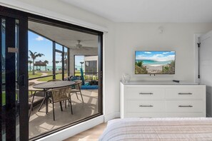 Une chambre dotée d’une grande porte-fenêtre coulissante donnant sur un balcon avec une table et des chaises, une commode blanche et un téléviseur fixé au mur.