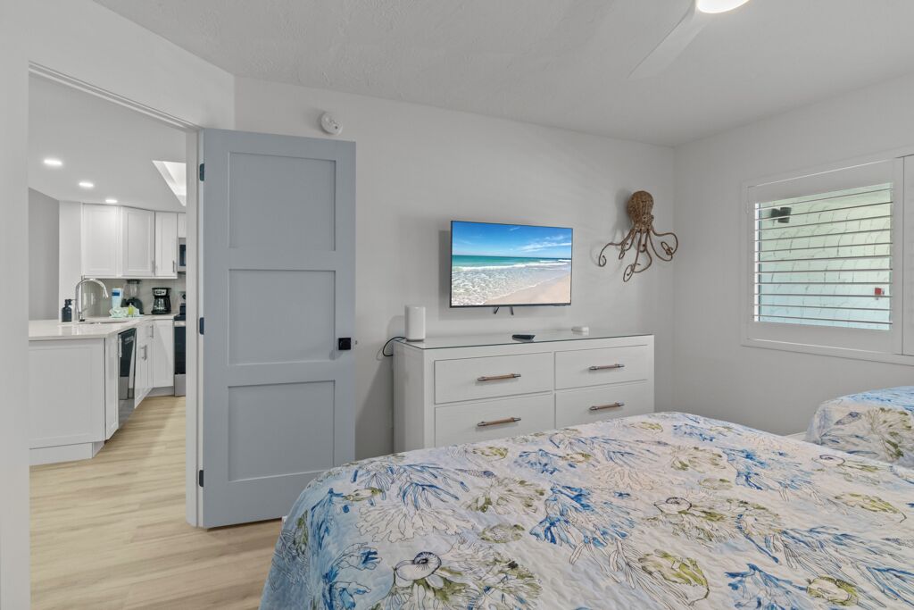 A bedroom with a bed, a dresser, a television, and a window with blinds.