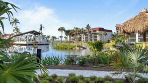 A resort with a central water feature, palm trees, and modern buildings with a thatched roof structure.