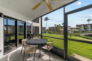 A balcony with a table and chairs, large windows, and a view of a golf course and buildings.