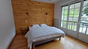 A bedroom with a wooden headboard, a large window with a view of the outdoors, and a bed with white bedding. - Authentic family home, 5 minutes from Saint-Lary-Soulan (Guchan)