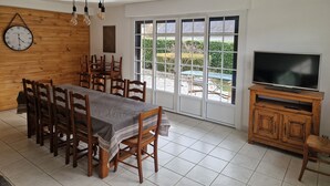 A dining area with a long wooden table and chairs, a clock on the wall, and a TV on a wooden cabinet. - Authentic family home, 5 minutes from Saint-Lary-Soulan (Guchan)