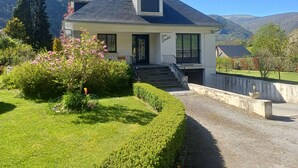 A two-story house with a dark roof, a front porch, and a staircase leading to the entrance. - Authentic family home, 5 minutes from Saint-Lary-Soulan (Guchan)