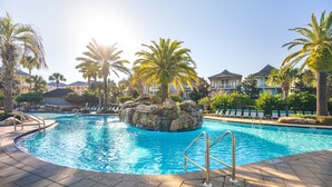 A swimming pool with a rock feature and palm trees, surrounded by a resort setting.