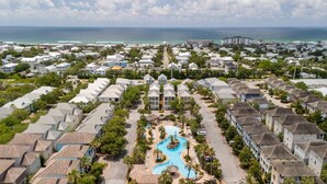 A resort with a central swimming pool, surrounded by residential-style buildings, and a view of the ocean.