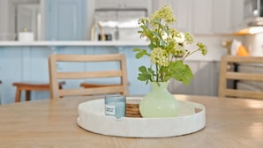 A kitchen with a white countertop, a wooden chair, a vase with flowers, and a candle on a tray.