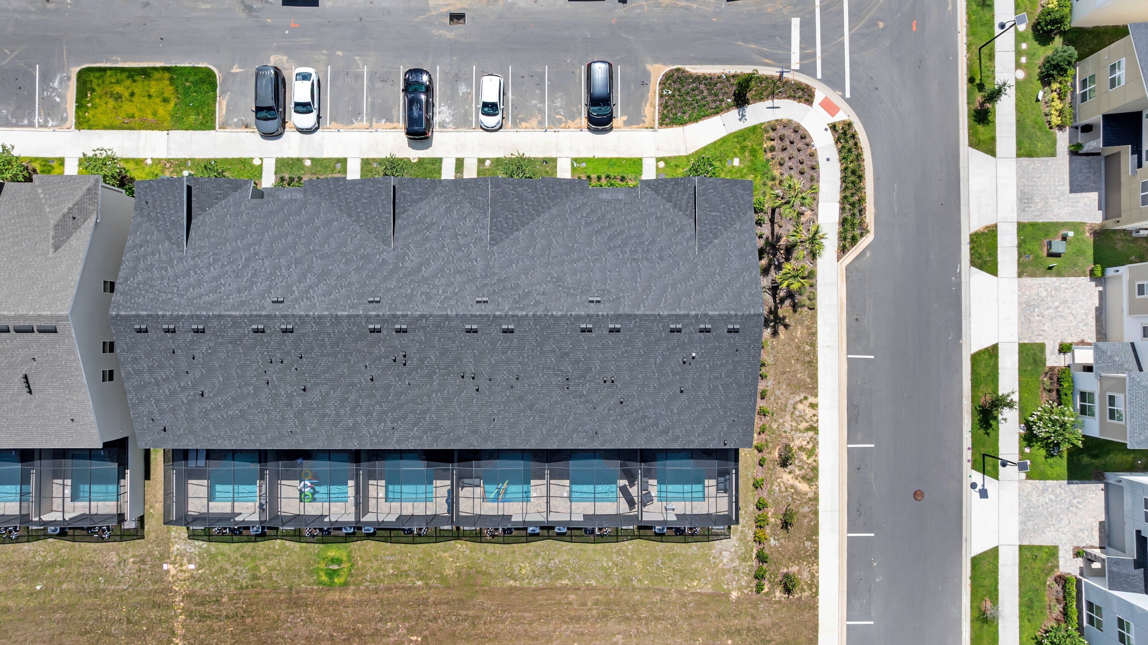 A modern building with a flat roof, multiple swimming pools, and a parking lot with several cars.