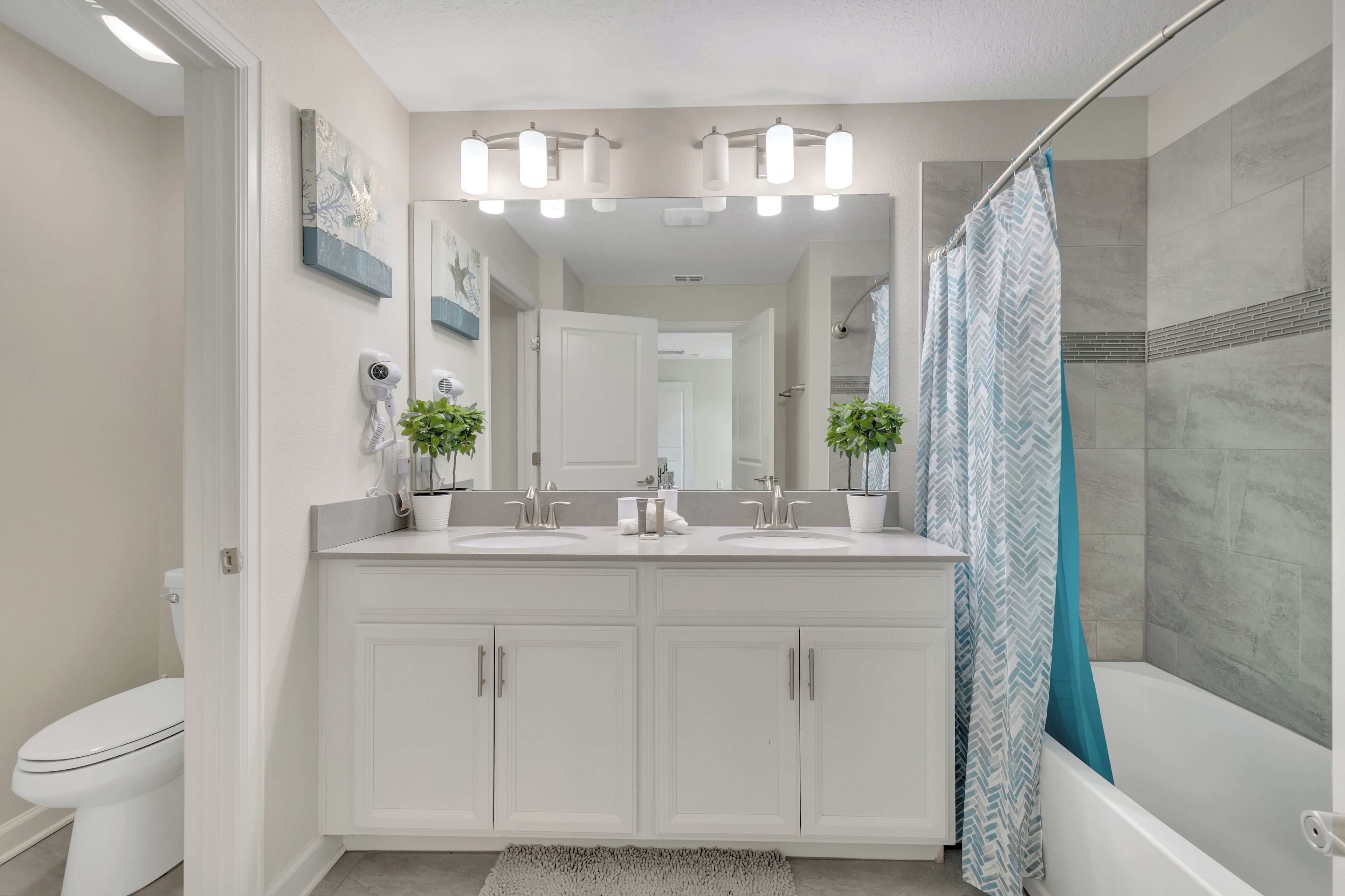 A modern bathroom with a double sink vanity, a shower with a blue and white chevron shower curtain, and a large mirror above the vanity.