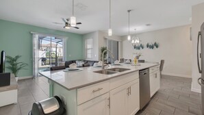 A modern kitchen with a large island, white cabinetry, and a view to the outside. - 1557 SD - Champions Gate Stylish Family Home (Four Corners)