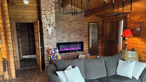 L’intérieur d’un chalet confortable en bois, avec une cheminée, un canapé gris et une décoration rustique.