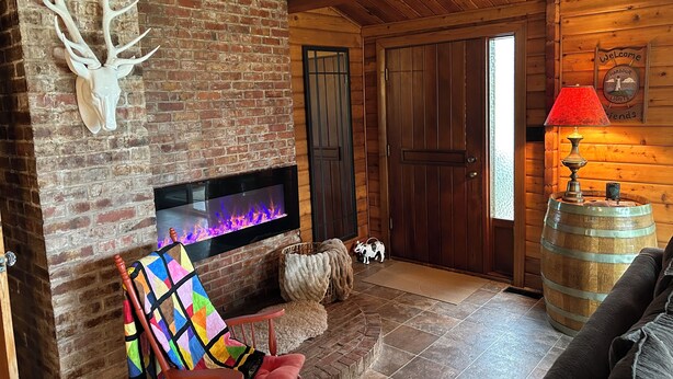 A rustic interior with a brick fireplace, a wooden door, a colorful quilted chair, and a wooden barrel. - Harbour Lights at New London Bay near Cavendish (Resort Mun. Stan.b.-Hope R.-B*)