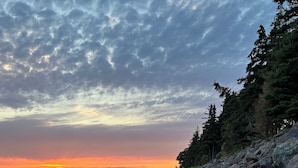 Une côte rocheuse, avec un coucher de soleil sur une étendue d’eau, le tout entouré d’arbres.