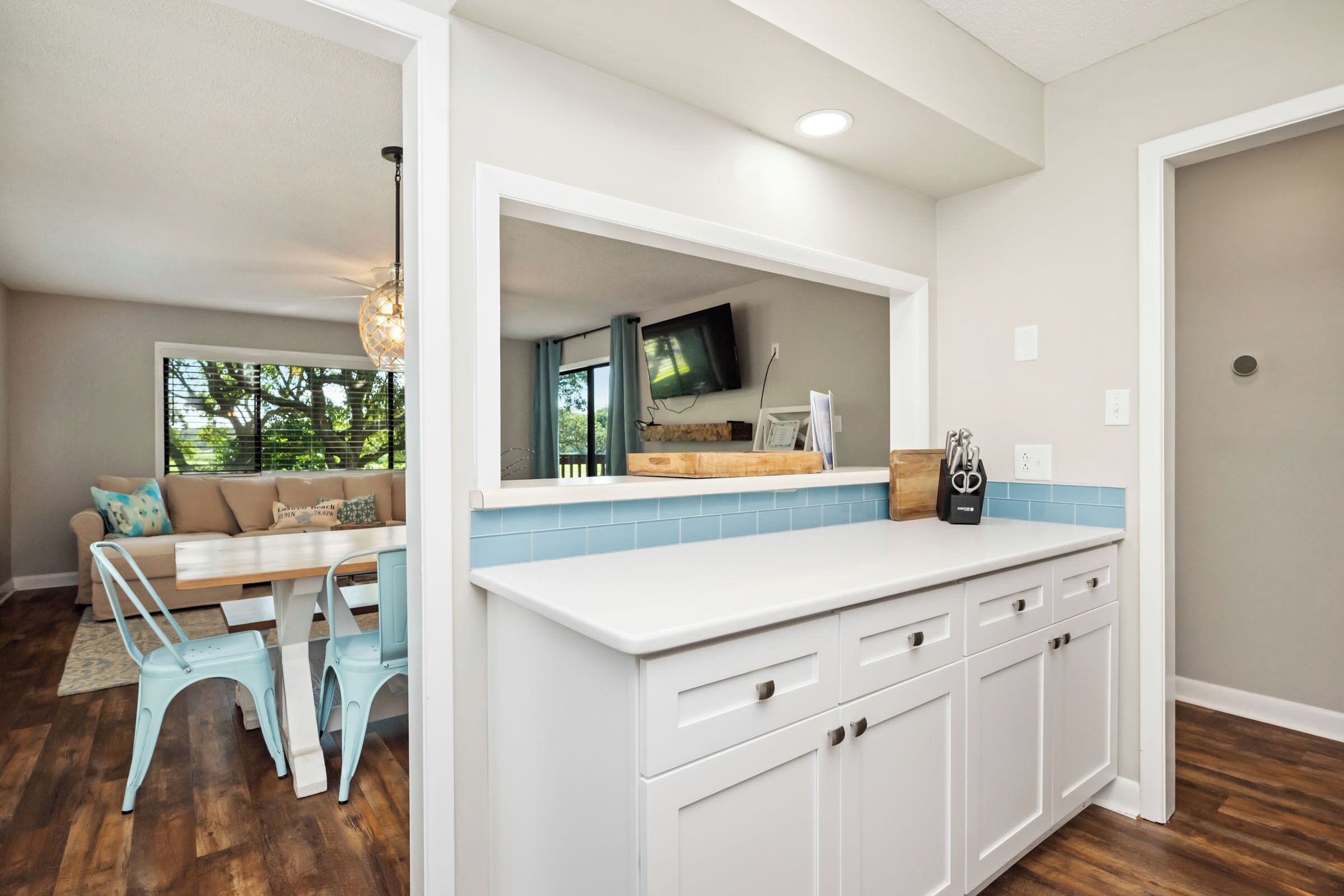 A modern kitchen with white cabinetry, a large island, and a dining area with a wooden table and blue chairs.