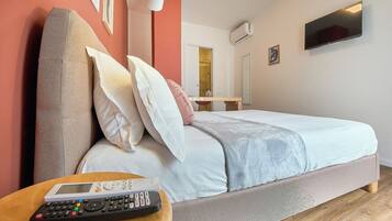 A bedroom with a bed, a bedside table with a remote control, a wall-mounted TV, and an air conditioning unit.