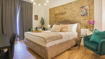 Ein Schlafzimmer mit einem großen Bett, einem grünen Sessel, Holzboden, Backsteinwand und einem Gemälde.