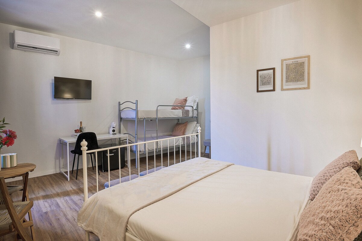 A bedroom with a bunk bed, a desk, a chair, and a TV mounted on the wall.