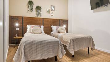 A bedroom with two beds, a wooden headboard, a small table, and a TV mounted on the wall.