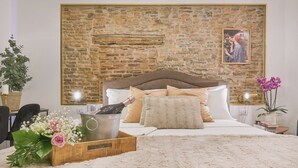 Une chambre avec un mur en pierre, un lit avec une literie blanche, une tête de lit en bois et une table de chevet avec une lampe.