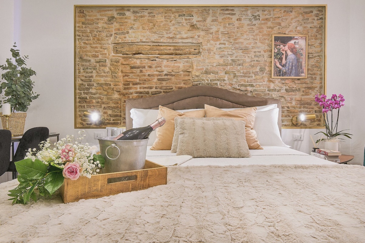 Ein Schlafzimmer mit Steinswand, einem Bett mit weißer Bettwäsche, einem Holz-Kopfteil und einem Nachttisch mit Lampe.