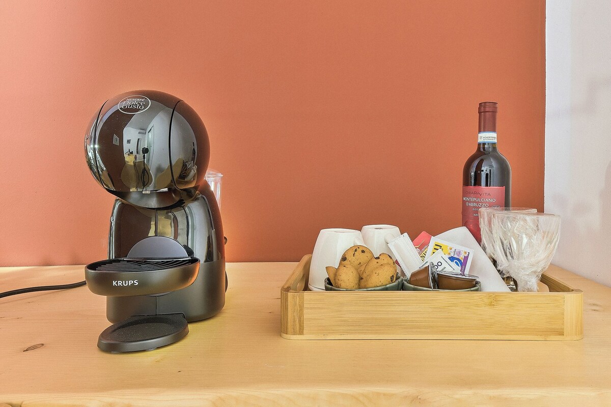 A coffee maker, a wine bottle, and a tray with cups and cookies on a wooden table.