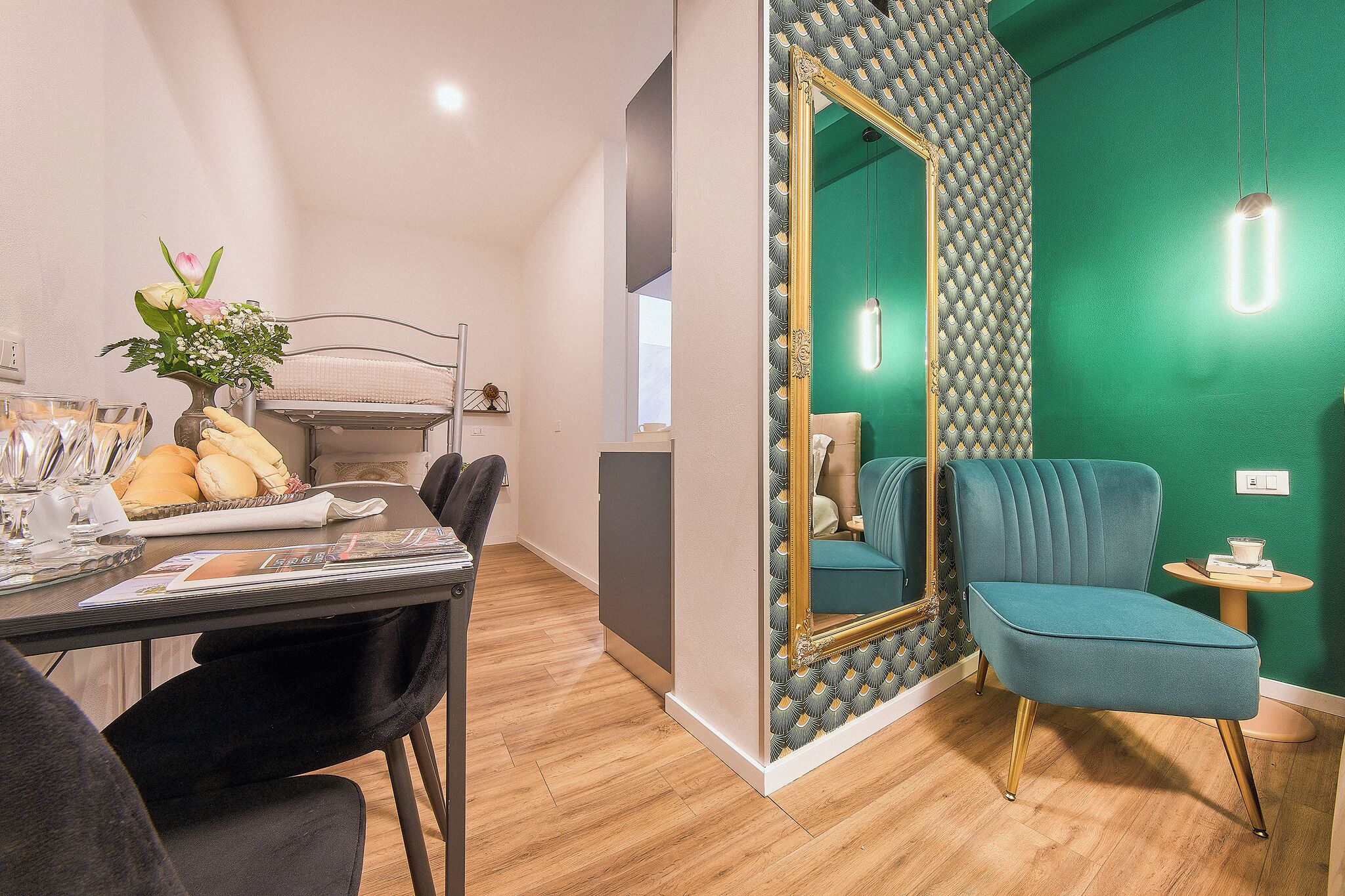 Een moderne kamer met een zithoek, een blauwgroene fauteuil en een grote spiegel met decoratieve lijst.