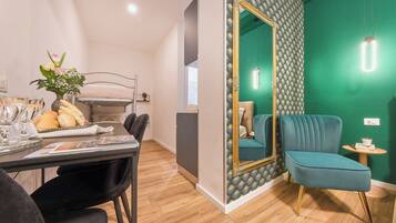Een moderne kamer met een zithoek, een blauwgroene fauteuil en een grote spiegel met decoratieve lijst.
