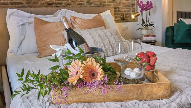 Un lit parfaitement fait, agrémenté d’une bouteille de champagne, de verres, de fraises et de fleurs, le tout disposé sur un plateau en bois.