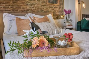 Una cama impecablemente hecha con una botella de champán, copas, fresas y flores sobre una bandeja de madera.