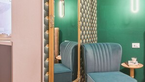 Une pièce avec un grand miroir, un fauteuil bleu rembourré et une petite table ronde sur laquelle se trouve une lampe.