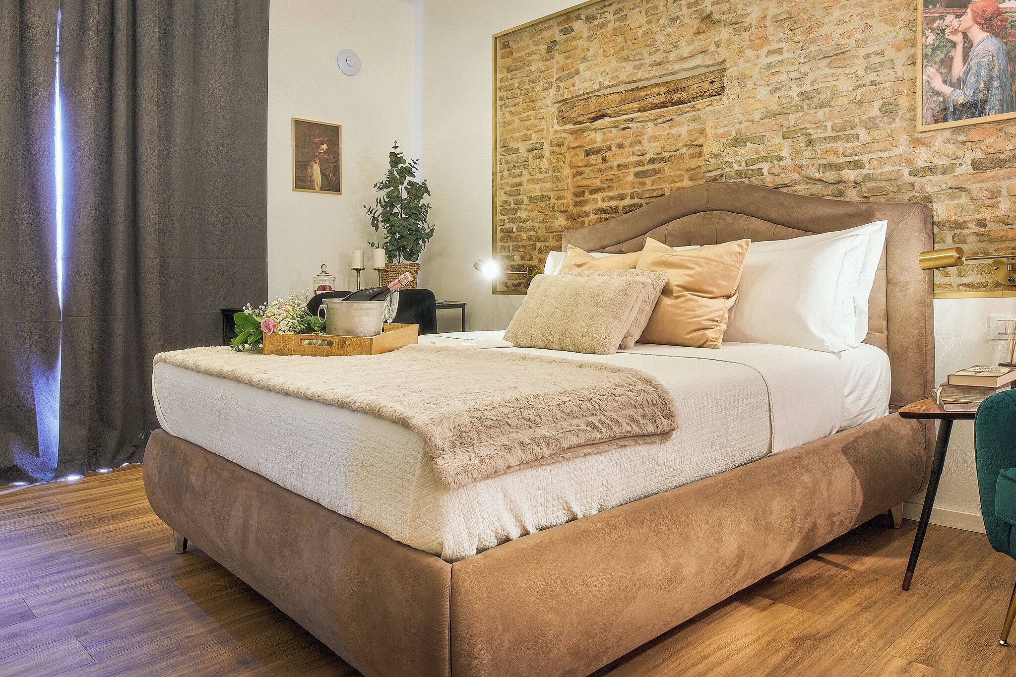 A bedroom with a large bed, a brick wall, and a small table with a lamp.