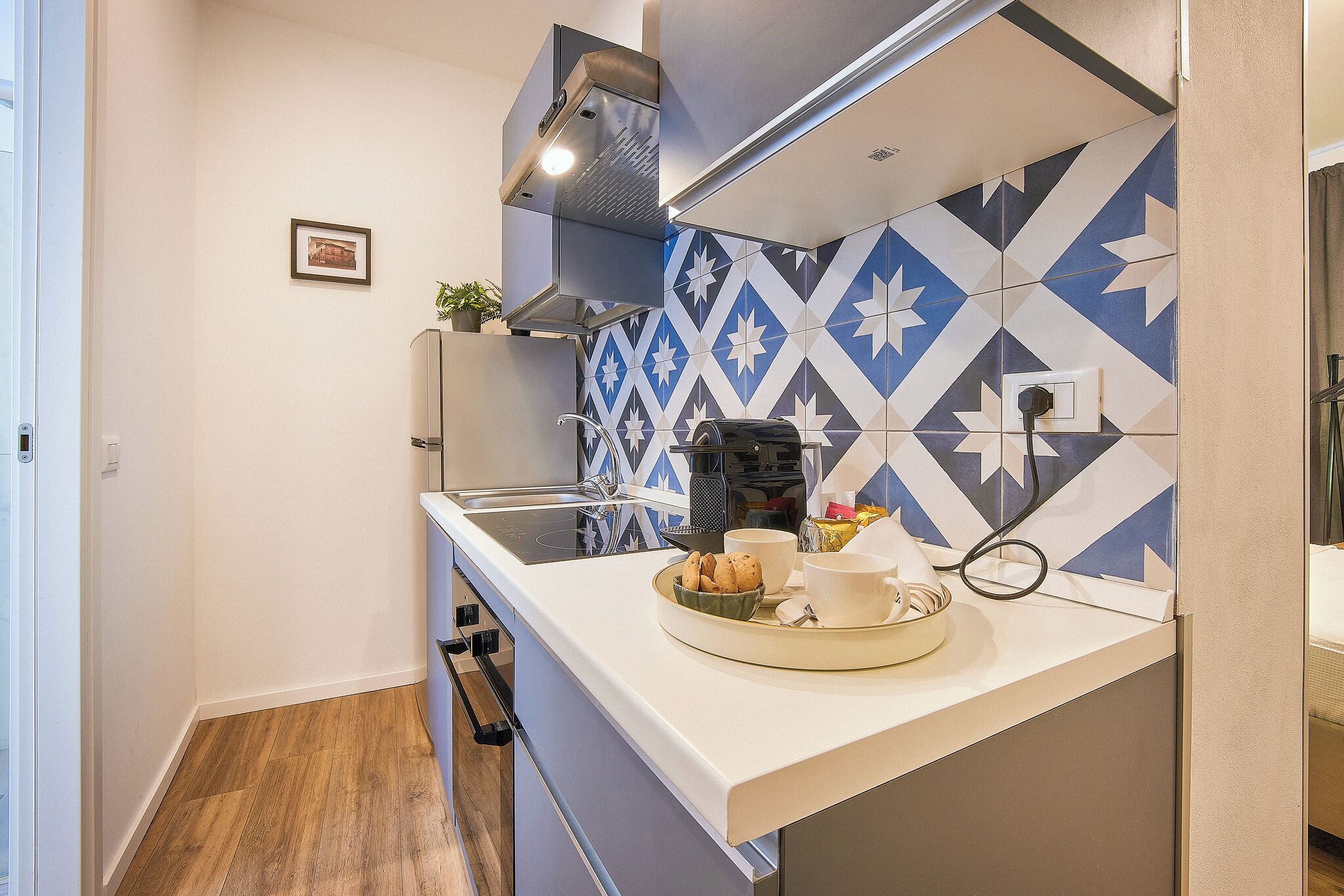 A compact kitchen with a modern design, featuring a white countertop, a built-in stove, and a patterned backsplash.