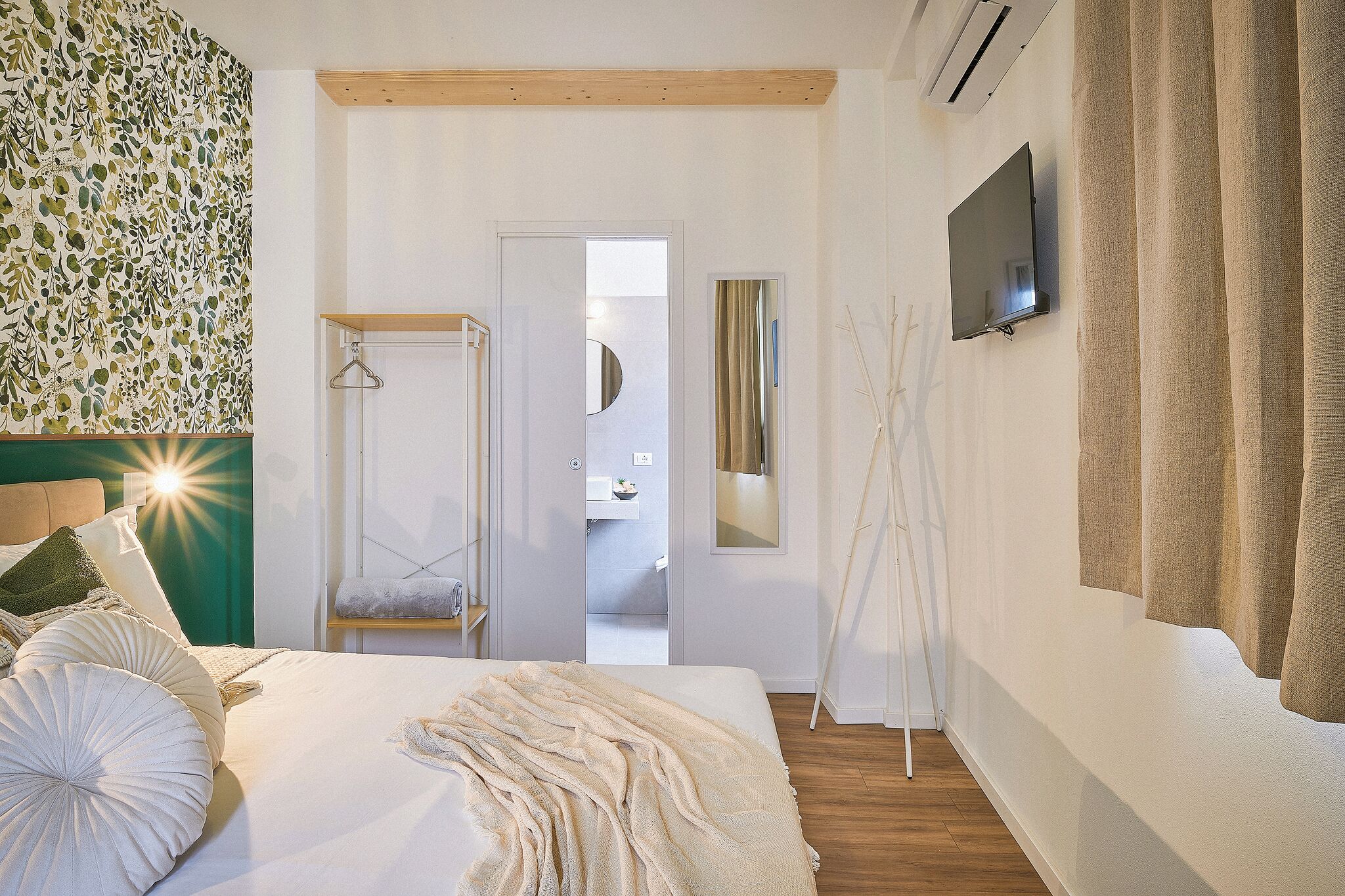 Un dormitorio con cama, televisión, espejo y puerta que da a un baño.