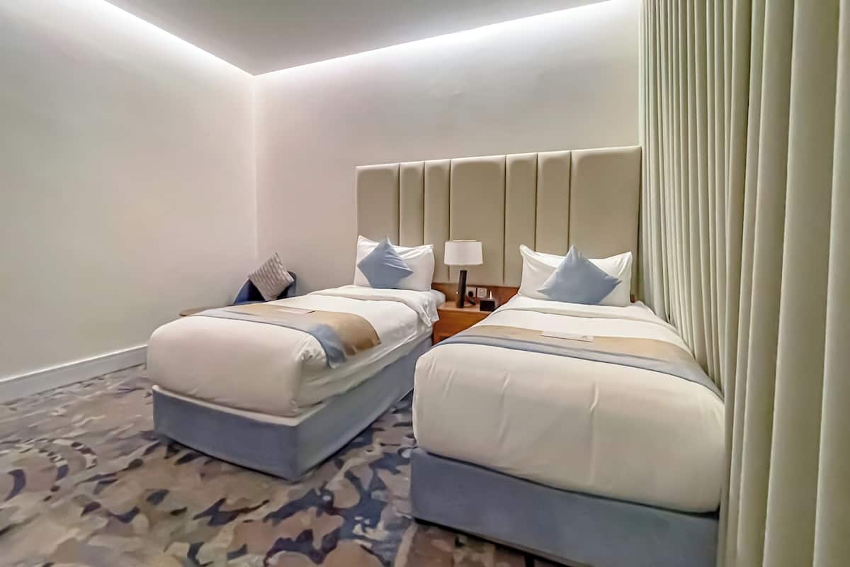 A hotel room with two beds, a patterned carpet, and a headboard with a light fixture.