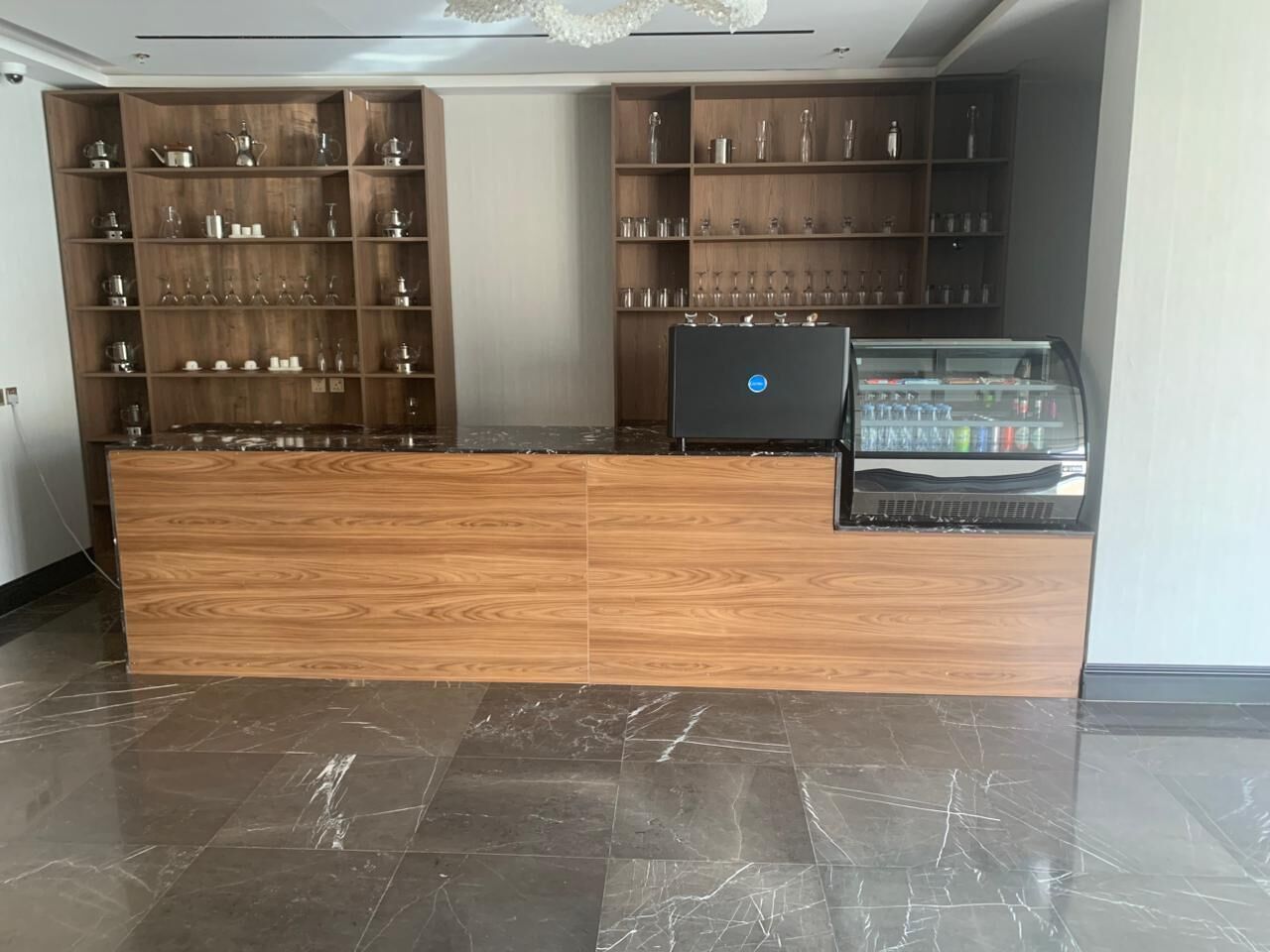 A reception desk with a laptop, shelves with glassware, and a coffee machine.