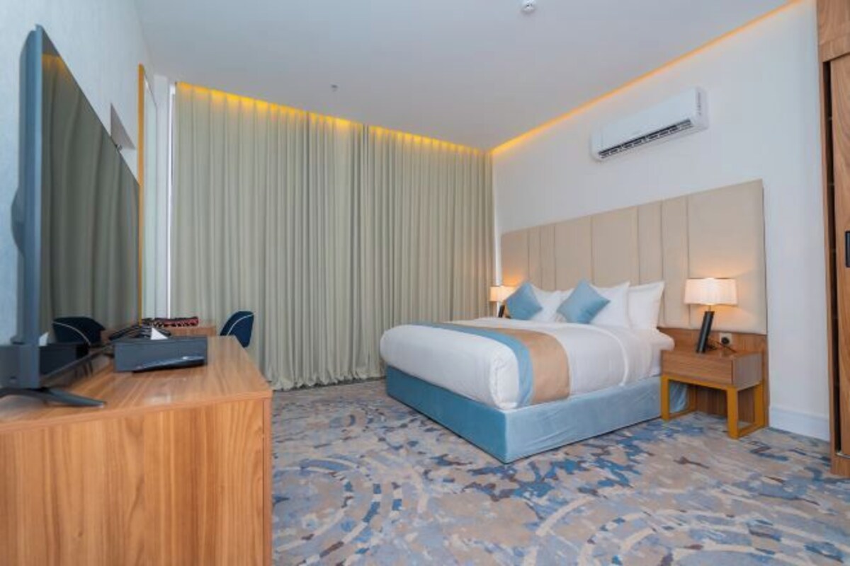 A hotel room with a bed, bedside tables, a desk, and a large mirror.