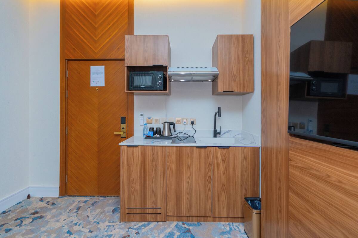 A compact kitchen with wooden cabinetry, a microwave, a kettle, and a sink.