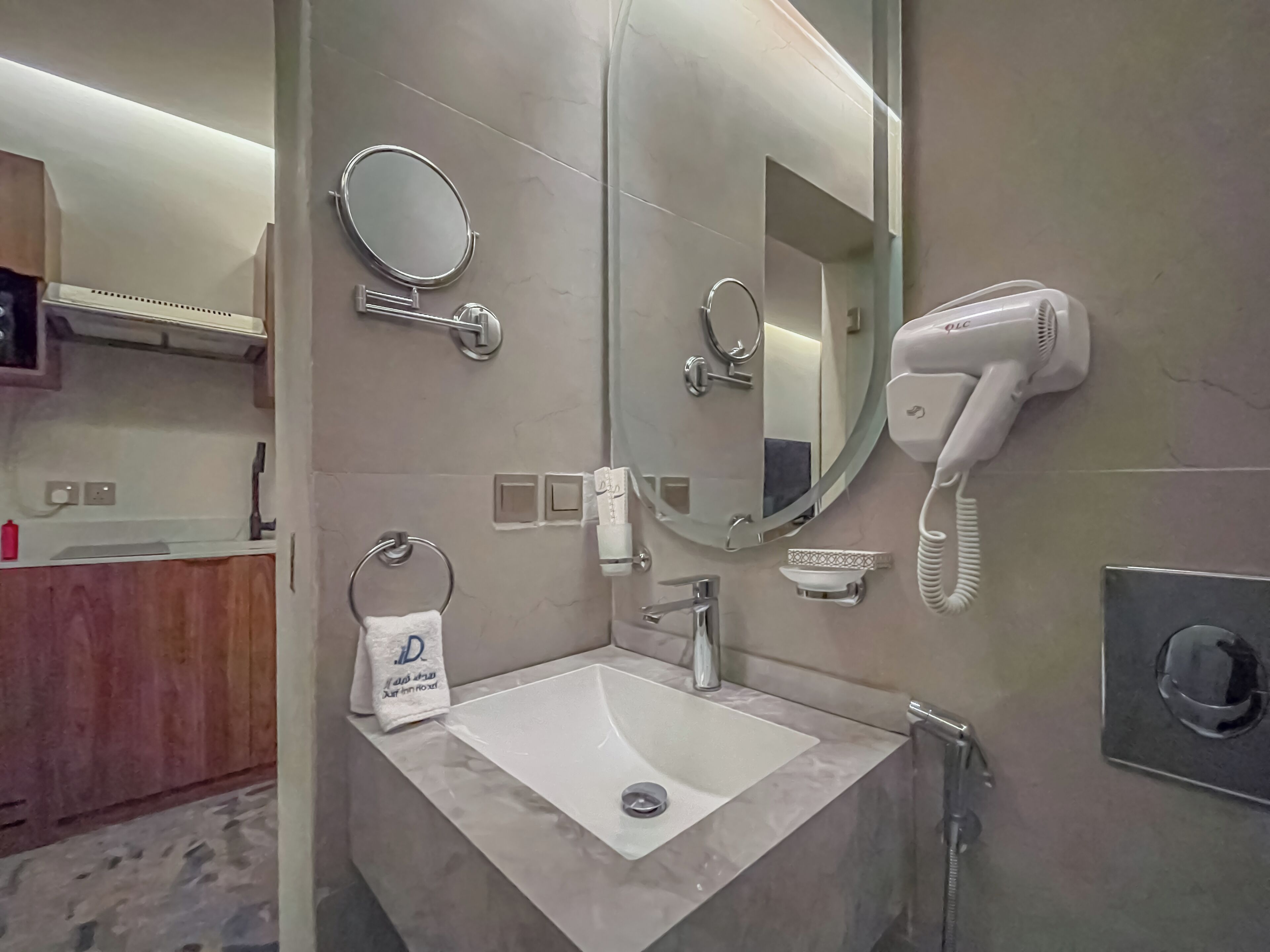 A bathroom with a sink, two mirrors, a hairdryer, and a towel dispenser.