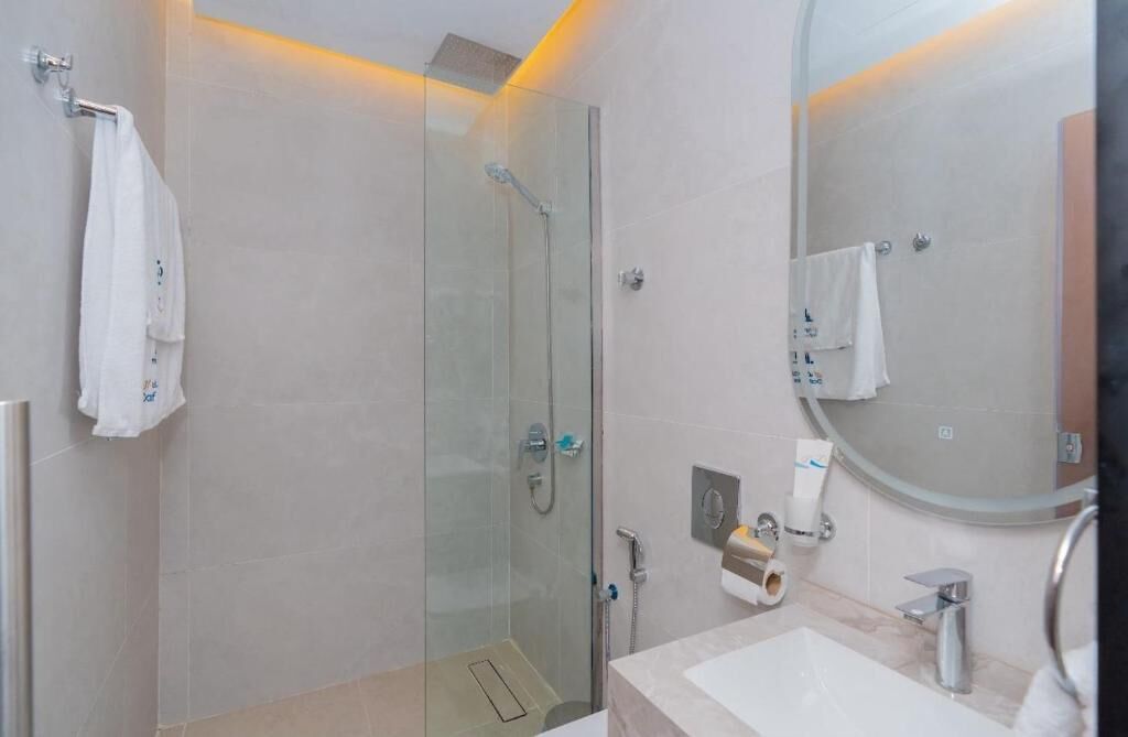 Een moderne badkamer met een douche met glazen wand, een ronde spiegel en een witte wastafel.