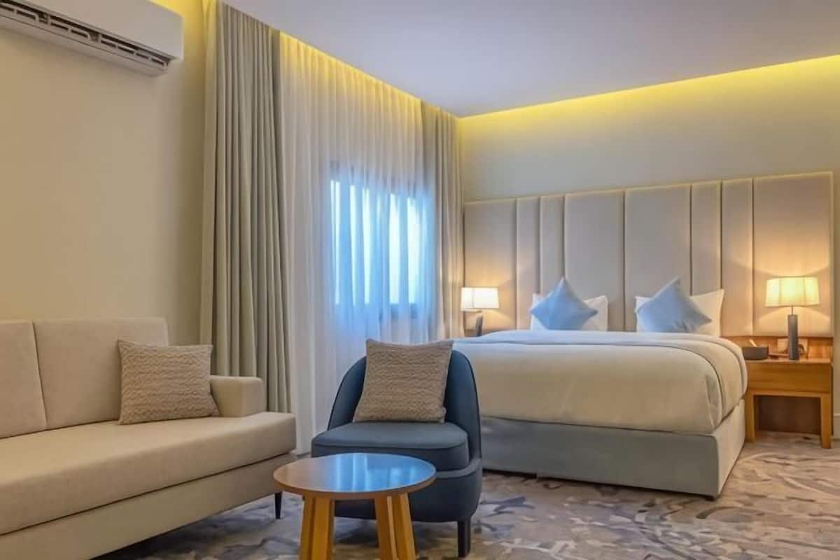 A hotel room with a bed, a sofa, a chair, a small table, and a nightstand with lamps.
