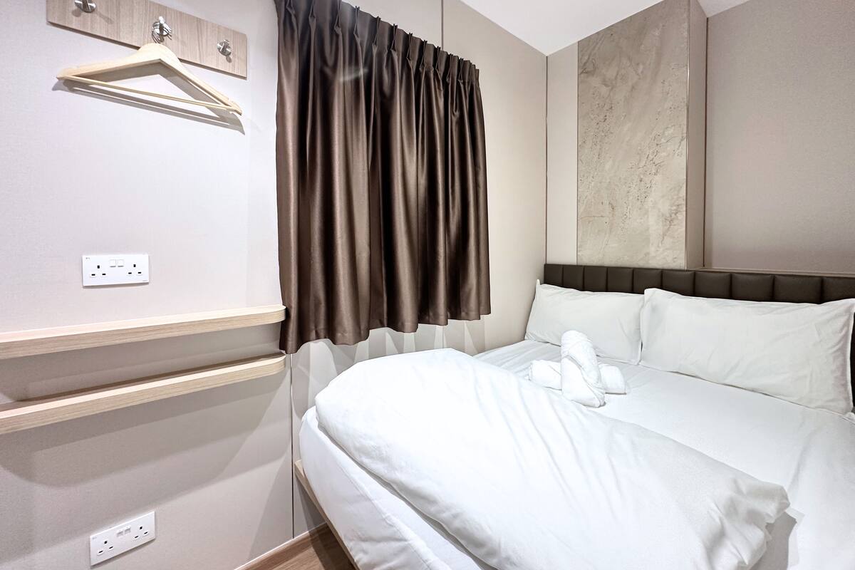 A hotel room with a bed, a wooden shelf, a wall-mounted light, and a power outlet.