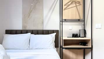Una habitación de hotel con una cama, un estante de madera con un hervidor y una percha para ropa.